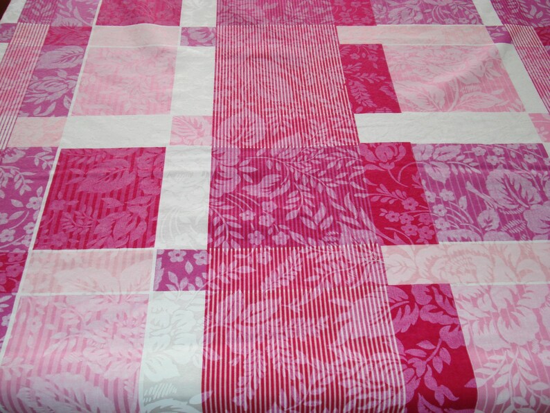 May include: A patchwork quilt with a mix of pink and white floral and striped designs. The quilt is made up of rectangular blocks, with different shades of pink and white, forming an attractive pattern. The floral patterns include roses and other botanical designs.