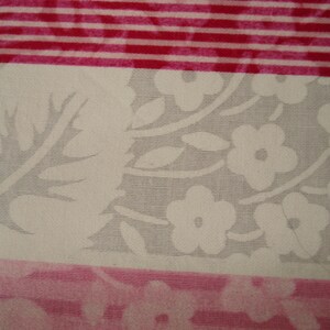 May include: Close-up of fabric with floral and striped patterns. The floral section has white flowers and leaves on a grey background. The striped sections are red and white.