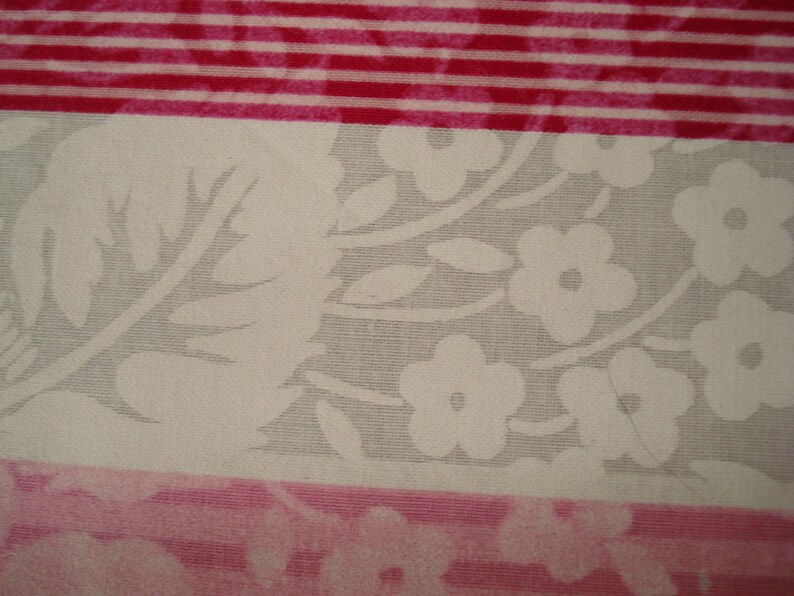May include: Close-up of fabric with floral and striped patterns. The floral section has white flowers and leaves on a grey background. The striped sections are red and white.