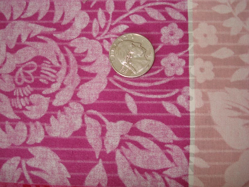 May include: Close-up of a pink fabric with a floral pattern and a coin. The fabric features large white floral designs and smaller flowers. The coin is silver and shows a profile.