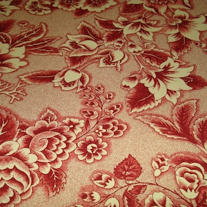May include: Close-up of a fabric with a floral pattern. The design features large, stylized flowers and leaves in shades of red and cream, set against a dotted background. The fabric has a vintage or antique aesthetic.