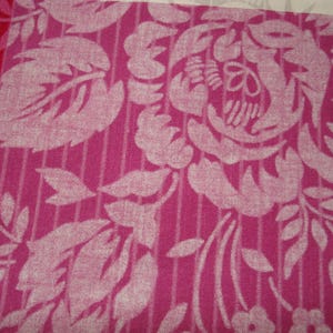 May include: Close-up of a floral fabric with a repeating pattern. The design features large, stylized white flowers and leaves against a pink background with vertical stripes. A section of red fabric is visible on the left.