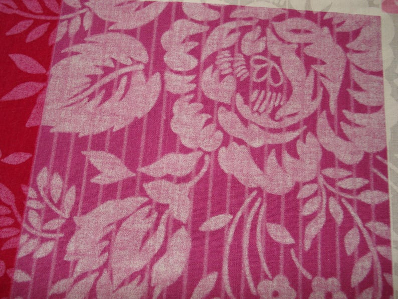 May include: Close-up of a floral fabric with a repeating pattern. The design features large, stylized white flowers and leaves against a pink background with vertical stripes. A section of red fabric is visible on the left.