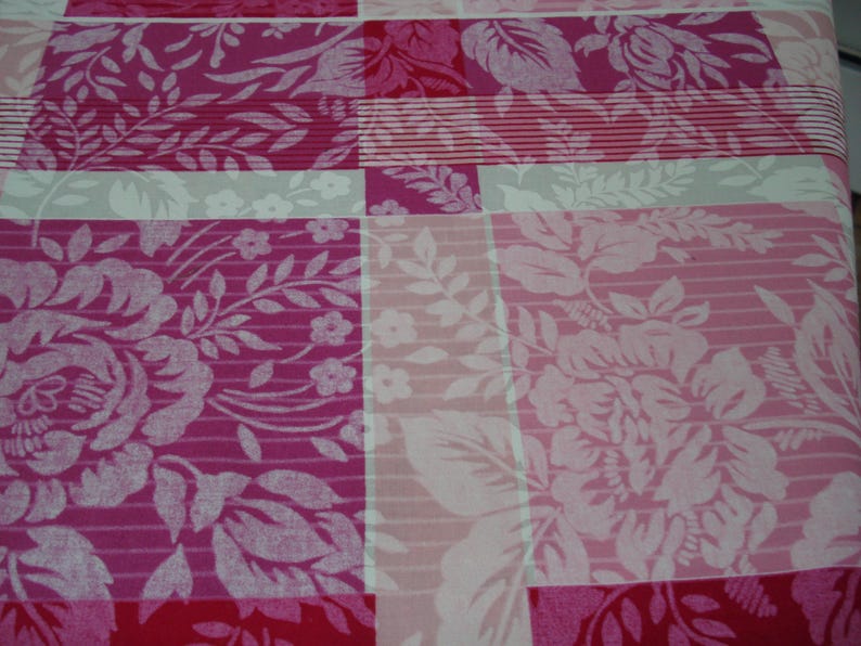 May include: Close-up of a fabric with a floral pattern in shades of pink, red, and white. The design features large rose and leaf motifs, arranged in a patchwork style with stripes and solid blocks.