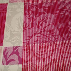 May include: A close-up of a textile with a patchwork design. The pattern features alternating squares of pink floral and striped patterns, and a gray floral design. The color palette includes shades of pink and white.