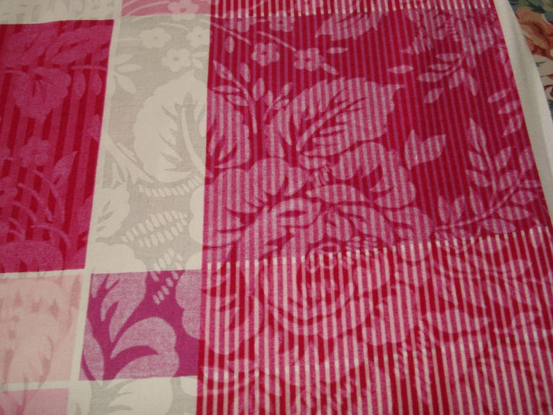 May include: A close-up of a textile with a patchwork design. The pattern features alternating squares of pink floral and striped patterns, and a gray floral design. The color palette includes shades of pink and white.
