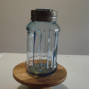 May include: A vintage blue glass jar with a metal lid. The jar has vertical ridges and a rounded bottom. The jar is sitting on a wooden stand.