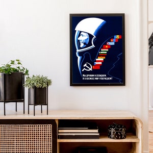 Może przedstawiać: Winietkowy plakat propagandowy Związku Radzieckiego przedstawiający astronautę w hełmie na niebieskim tle. Plakat zawiera tekst "Мы дружим и создаем, и в космос мир утверждаем!" kt&oacute;ry tłumaczy się jako "Jesteśmy przyjaci&oacute;łmi i tworzymy, i potwierdzamy pok&oacute;j w kosmosie!" Plakat zawiera r&oacute;wnież szereg flag reprezentujących r&oacute;żne kraje.