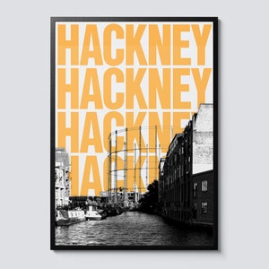 Op de afbeelding: Een zwart-witfoto van een kanaal in Londen met een grote gashouder op de achtergrond. Het woord "Hackney" wordt in fel oranje herhaald over de afbeelding.