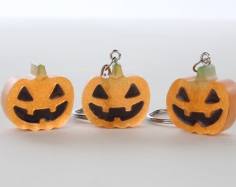 Può includere: Tre portachiavi a forma di zucca arancione con glitter e facce di zucca nere.