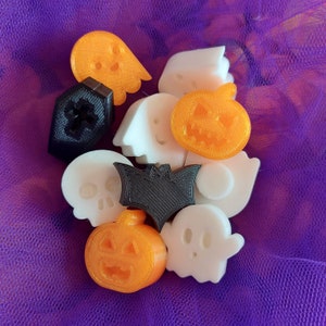 Pode incluir: Uma coleção de decorações de Halloween feitas de plástico branco, preto e laranja. As decorações incluem fantasmas, abóboras e uma caveira.