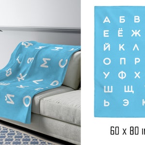 May include: A light blue fleece blanket with a white Cyrillic alphabet pattern. The blanket is 60 inches by 80 inches.