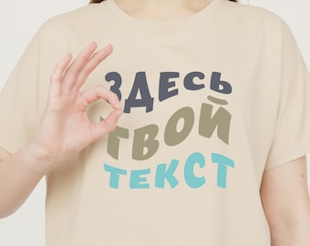 以下が含まれることがあります： ベージュのTシャツに、カラフルでスタイリッシュなフォントで「ЗДЕСЬ ТВОЙ ТЕКСТ」というテキストが書かれています。