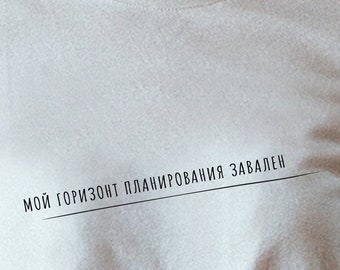 以下が含まれることがあります： 黒い文字で「мой горизонт планирования завален」と書かれた白いTシャツ。