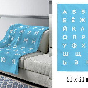 May include: A light blue fleece blanket with the Cyrillic alphabet printed in white. The blanket is 50 by 60 inches.