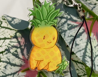 May include: A yellow and green pineapple-shaped charm with a smiling face, attached to a black string with a silver clasp.