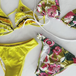 May include: Two bikini tops and two bikini bottoms. One bikini set is yellow with brown and white trim and sequins. The other bikini set is green with pink and white floral print.