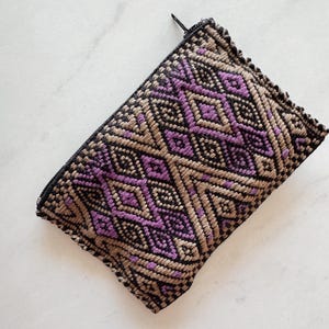 May include: A small, zippered pouch with a geometric pattern in shades of black, brown, and purple. The pattern is woven into the fabric and features a repeating diamond shape.