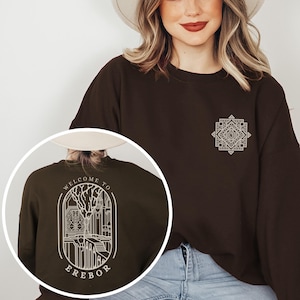 May include: A brown sweatshirt with a white graphic on the front and a white graphic on the back. The front graphic is a geometric design. The back graphic is a circular design with the text "Welcome to Erebor".