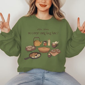 Op de afbeelding: Een groen sweatshirt met een afbeelding van een ontbijt en de tekst "Why don't we have second breakfast?" in een speels lettertype.
