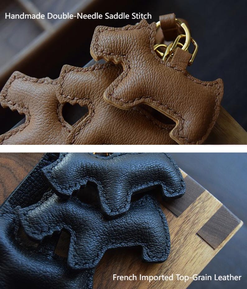 K&ouml;nnte beinhalten: Nahaufnahme von zwei ledernen Schl&uuml;sselanh&auml;ngern in Hundeform. Einer ist braun mit einem goldfarbenen Verschluss, der andere ist schwarz. Die Schl&uuml;sselanh&auml;nger sind mit einem doppelten Sattelstich gefertigt. Der Text "Handmade Double-Needle Saddle Stitch" und "French Imported Top-Grain Leather" sind sichtbar.