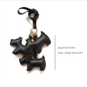 K&ouml;nnte beinhalten: Schwarzer Leder-Schl&uuml;sselanh&auml;nger in Hundeform mit goldenem Ring und schwarzem Riemen. Der Schl&uuml;sselanh&auml;nger zeigt drei Hundesilhouetten, jede etwa 9 cm hoch. Der Riemen ist etwa 16 cm lang.