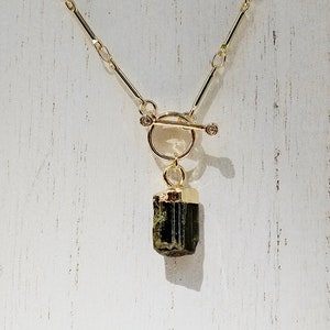 May include: A gold chain necklace with a toggle clasp and a dark green crystal pendant.