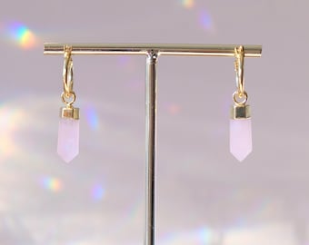 May include: A pair of gold hoop earrings with a pink crystal pendant hanging from each hoop.
