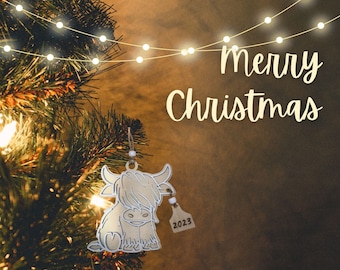 May include: A digital file for a Christmas ornament featuring a cute Highland cow with a 2023 tag. The ornament is hanging on a Christmas tree with lights. The text "Merry Christmas" is written in white on a brown background. The text "DIGITAL FILE SVG-PDF-PNG" is written in white on a black background.