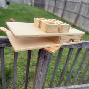 May include: A multi-tiered, unfinished wooden serving tray with a drawer and four small square containers. The tray is made of light-coloured wood and is designed for serving food or displaying items. The drawer has a small wooden knob.