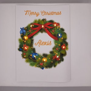 K&ouml;nnte beinhalten: Weihnachtliches Bild mit einem festlichen Kranz, einem roten Bogen und Ornamenten. &Uuml;ber dem Kranz steht &bdquo;Merry Christmas&ldquo;, und der Name &bdquo;Alexis&ldquo; befindet sich in der Mitte.