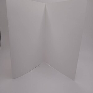 K&ouml;nnte beinhalten: Eine leere, wei&szlig;e, gefaltete Karte, die aufrecht steht. Die Karte ist in der Mitte gefaltet, wodurch eine V-Form entsteht. Die Karte befindet sich auf einem wei&szlig;en Hintergrund.