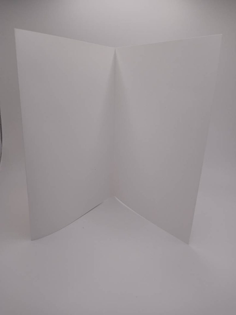 K&ouml;nnte beinhalten: Eine leere, wei&szlig;e, gefaltete Karte, die aufrecht steht. Die Karte ist in der Mitte gefaltet, wodurch eine V-Form entsteht. Die Karte befindet sich auf einem wei&szlig;en Hintergrund.