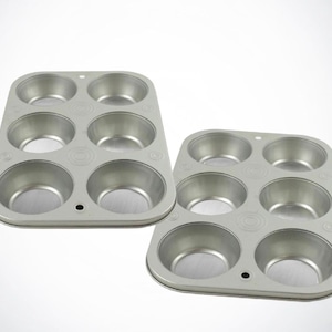 May include: Two silver-colored, six-cup muffin pans. Each pan has six round cups and a rectangular shape. The pans are made of metal and are designed for baking muffins or cupcakes.