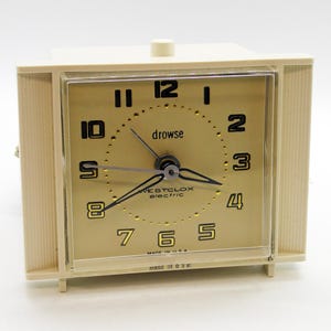 May include: Cream-colored vintage Westclox electric alarm clock. The clock has a square face with black numerals and hands, and the word "drowse" is printed above the center. The clock is marked "Made in U.S.A."