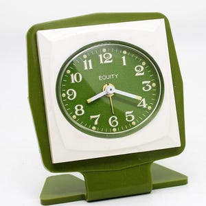 May include: A green and white vintage alarm clock with a green face and white numbers. The clock says "EQUITY" on the face.