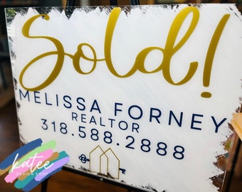 May include: A white sign with gold lettering that says "Sold!"  The sign also includes the text "Melissa Forney Realtor 318.588.2888" in blue lettering.