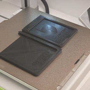 May include: Two black rectangular 3D-printed trays with text and a logo are displayed on a textured, metallic surface. One tray is open, and the other is closed. The text on the trays includes "KPSHIP.COM" and "1088194".