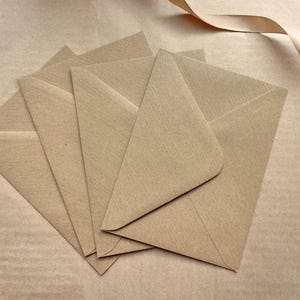 May include: A collection of five kraft paper envelopes fanned out, with a light brown ribbon in the upper right corner. The envelopes are arranged to show their triangular shape and the texture of the paper.