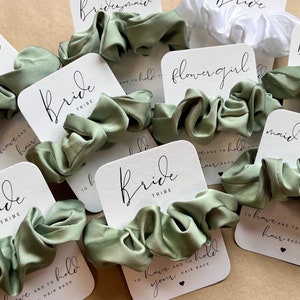 Peut inclure: Ensemble de chouchous en satin vert avec des cartes blanches qui disent "Bride Tribe", "Maid of Honor", "Flower Girl", et "To have and to hold your hair back".