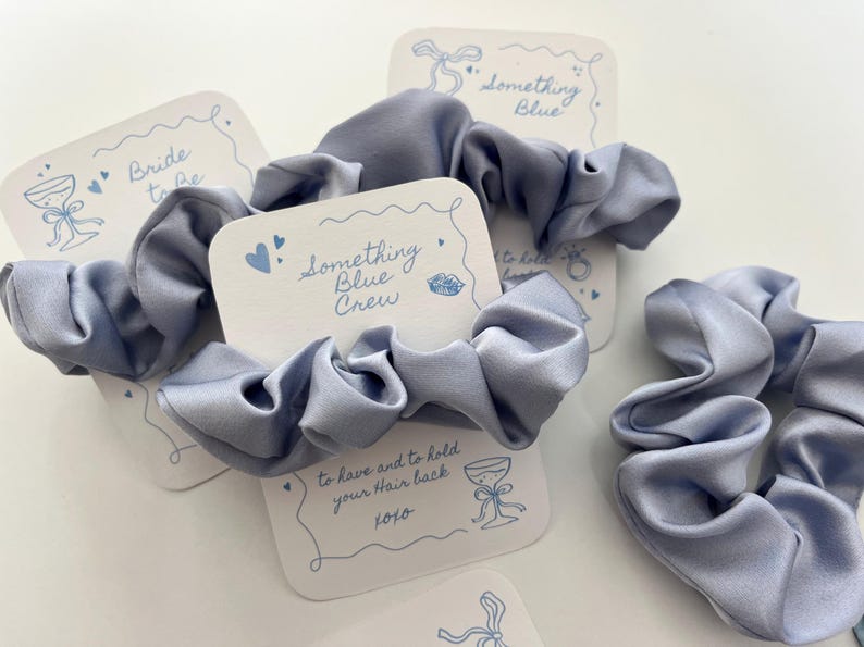 Puede incluir: Varios coleteros de sat&eacute;n azul claro se muestran con peque&ntilde;as tarjetas blancas. Las tarjetas tienen ilustraciones azules y el texto "Bride to be", "Something Blue Crew" y "to have and to hold your hair back xoxo".