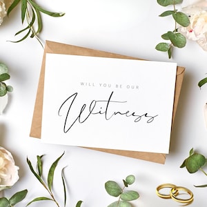 May include: A white card with the text "WILL YOU BE OUR Witness" in black script, on a brown envelope. The card is surrounded by white flowers, green leaves, and two gold wedding rings.