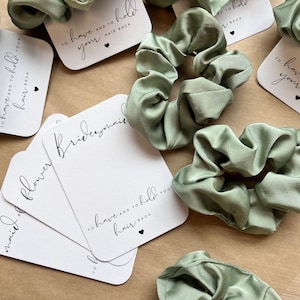 Peut inclure: Ensemble de quatre chouchous en satin vert avec des cartes blanches qui disent "To have and to hold your hair back" et "Bridesmaid" et "Maid of Honor" et "Flower Girl".