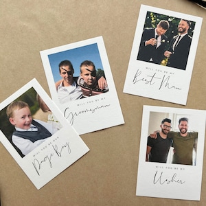 May include: Four white cards with photographs and text on a brown surface. The cards read "Will you be my Best Man", "Will you be my Groomsman", "Will you be our Page Boy", and "Will you be my Usher". Each card has a different photograph.