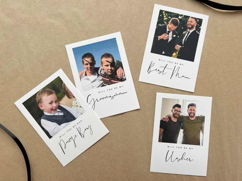 May include: Four white cards with photographs and text on a brown surface. The cards read "Will you be my Best Man", "Will you be my Groomsman", "Will you be our Page Boy", and "Will you be my Usher". Each card has a different photograph.