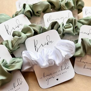 Peut inclure: Un ensemble de chouchous pour cheveux avec des cartes qui disent "Bride Tribe", "Bride", "Maid of Honor", "Bridesmaid" et "Flower Girl". Les chouchous sont en satin vert et blanc.