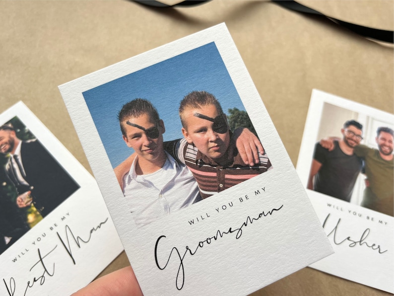 May include: White invitation cards with photos and text. One card says "Will you be my Groomsman" with a photo of two boys wearing eye patches. Other cards say "Best Man" and "Usher".