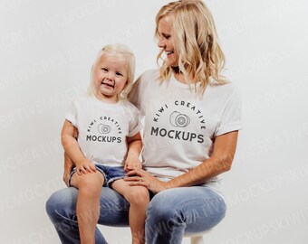May include: A white t-shirt with the text "Kiwi Creative Mockups" and a graphic of kiwi fruit. A woman and a child are wearing the shirts.
