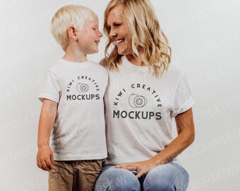 May include: Two white t-shirts with the text "KIWI CREATIVE MOCKUPS" and a kiwi fruit graphic. One shirt is worn by a child in khaki pants, the other by an adult in blue jeans.