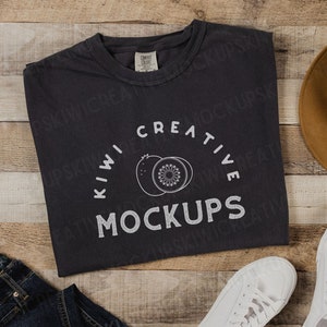 May include: A dark grey t-shirt with a white graphic design of two kiwi fruit and the text "Kiwi Creative Mockups".